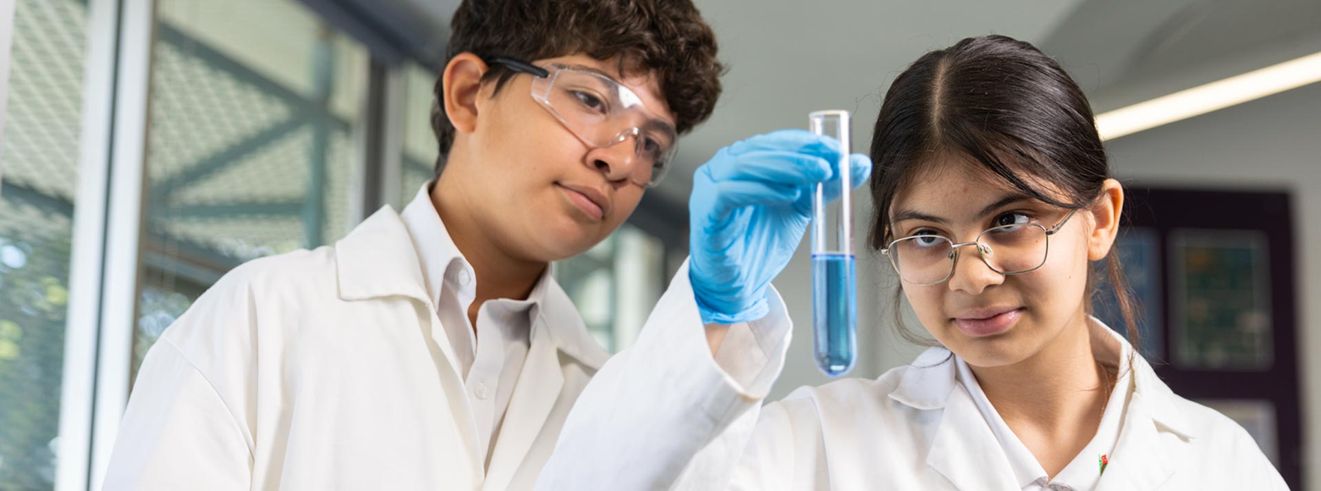 Two Delany College Granville science students holding a test tube full of blue liquid.