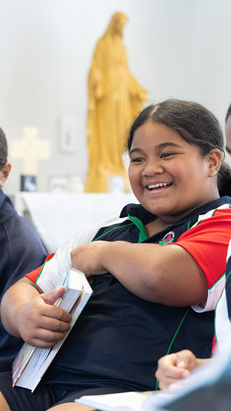 Happy student in Religion class. She is holding a Bible and a statue of Jesus is in the background