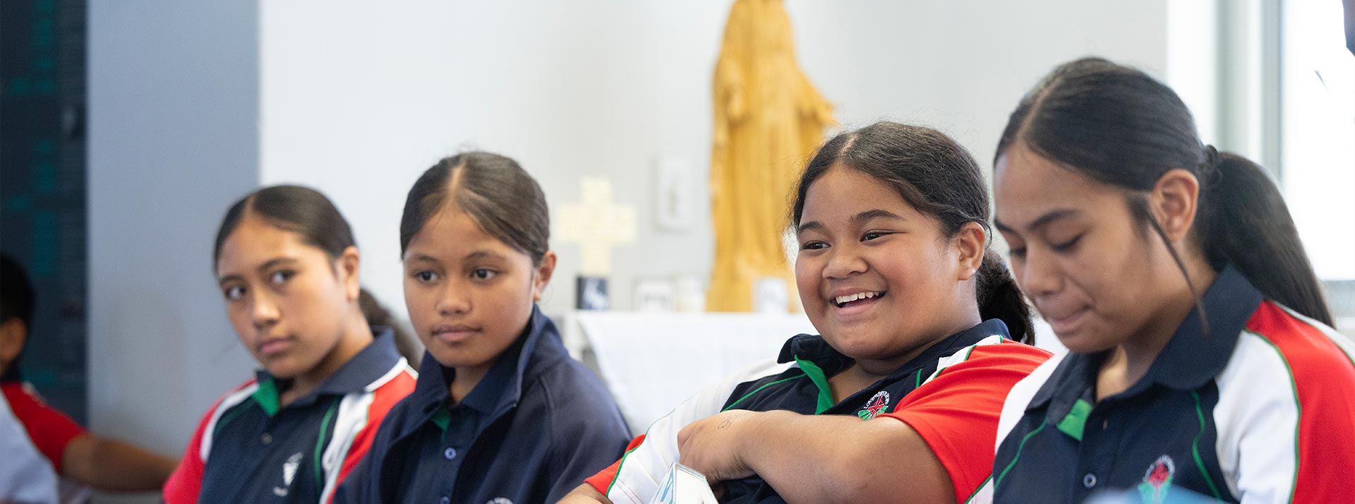 Happy student in Religion class. She is holding a Bible and a statue of Jesus is in the background