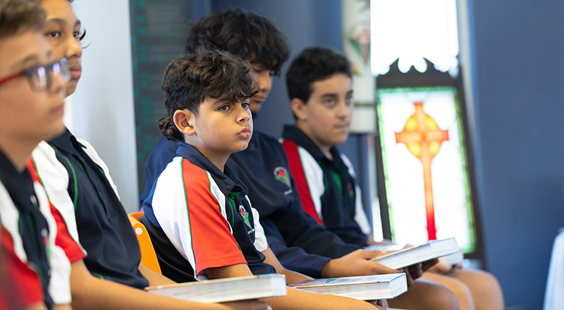 Students in Religion Class reading from Bible. Stained glass religious symbols are in the background.