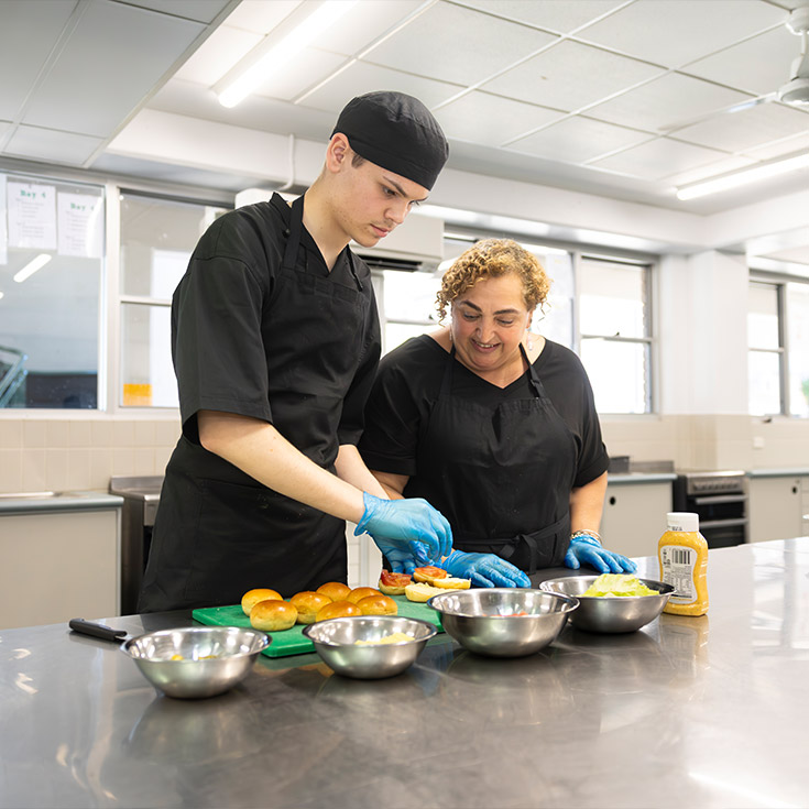 Food Tech teacher assisting Delany College Granville students with preparing hamburgers